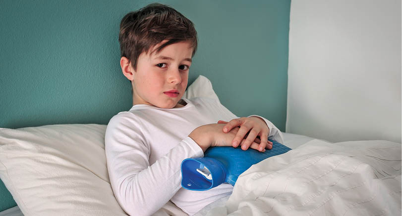 Young caucasian child is in bed sick with a cold holding a hot water bottle to his belly 