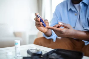 African man is sitting at the sofa at the home and taking blood from his finger due to diabetes. The daily life of a man of African-American ethnicity with a chronic illness who is using glucose test.