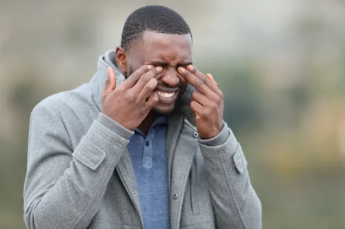Stressed man with black skin scratching his eyes in winter.