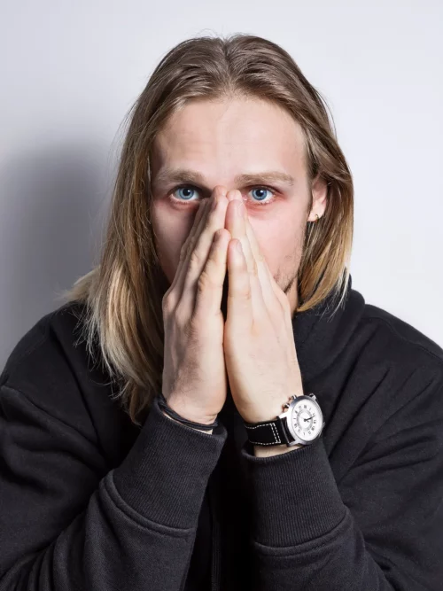 Long-haired blond man with his hands over his nose