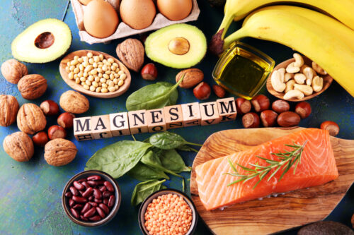 Products containing magnesium: bananas, almonds, avocado, nuts and spinach and eggs on table.