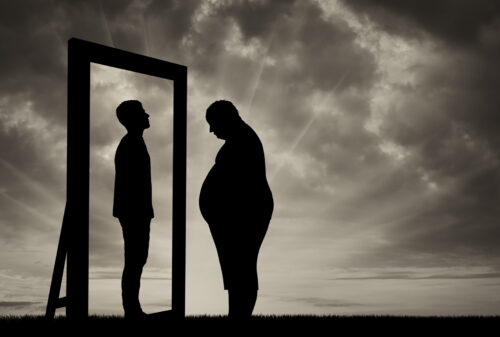 obese man looking at a reflection of a younger man in a mirror